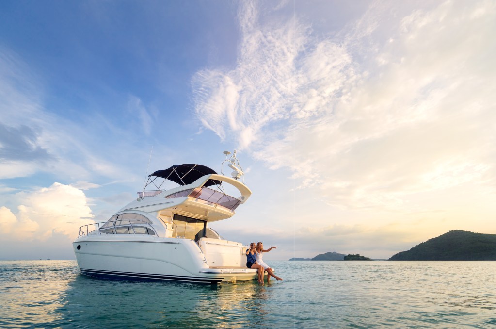 Friendship and luxury vacation. Two happy young women sitting on the yacht deck looking and pointing away sailing the sea.