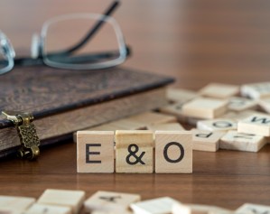 the acronym e&amp;o for errors and omissions insurance word or concept represented by wooden letter tiles on a wooden table with glasses and a book