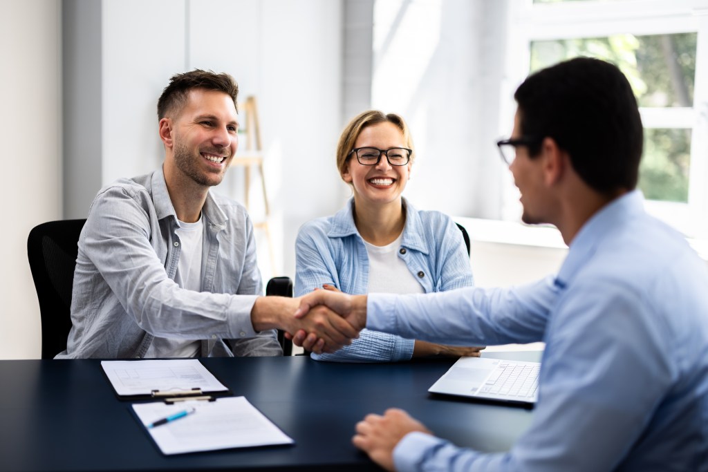 Young couple signing rental contract with real estate agent at apartment viewing, discussing financial plan and insurance with advisor.