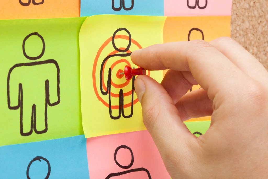 Hand pinning a sticky note in the center of a customer target on cork board